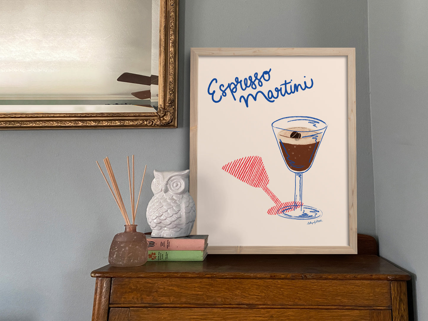 Framed artwork of an Espresso Martini with a glass and straw on a wooden book cabinet.